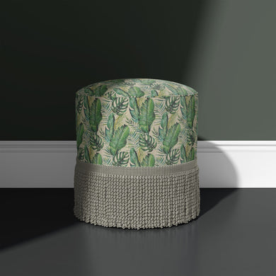 Amazon Leaf green upholstery fabric upholstered onto a round stool with fringe, shown against a dark green wall