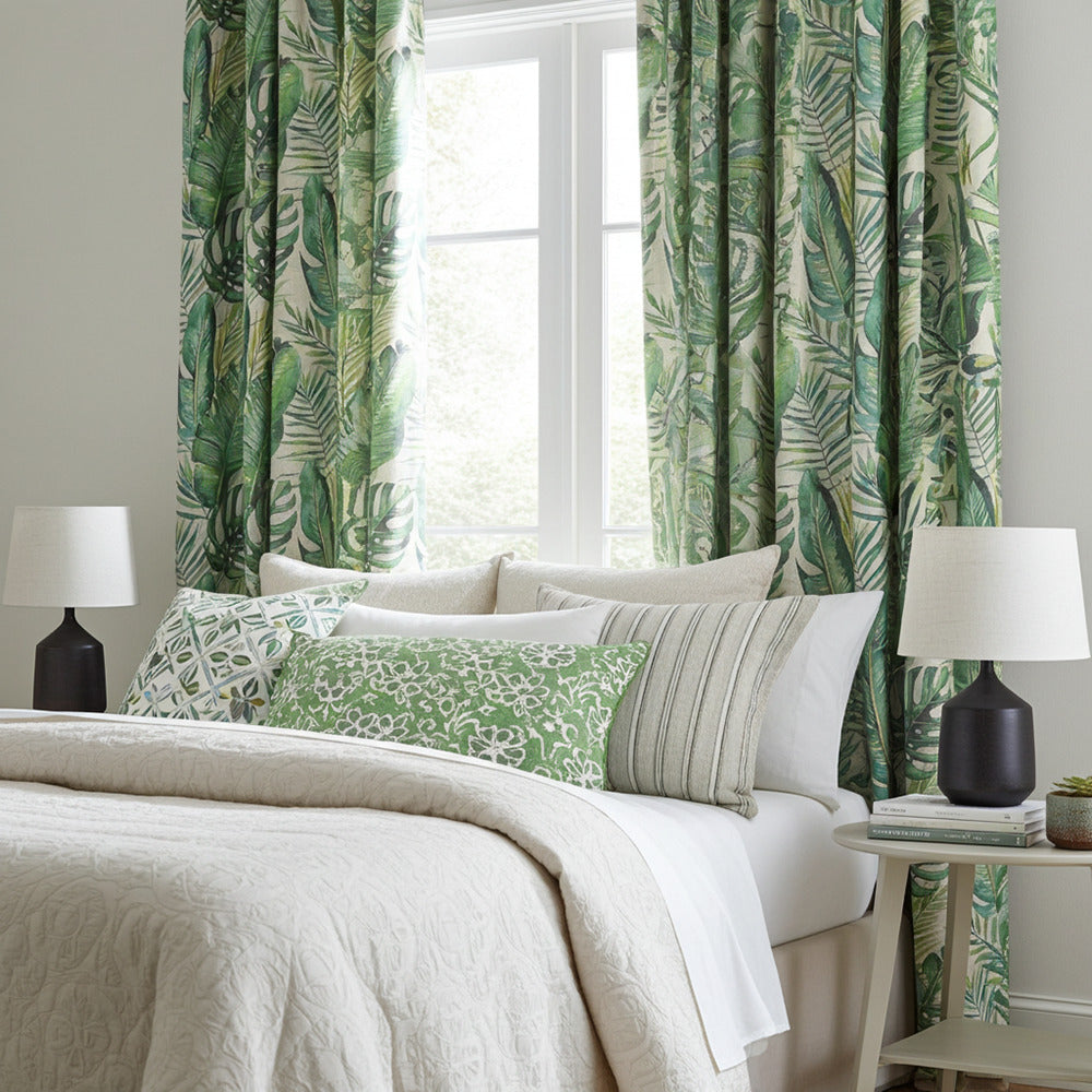 Jungle leaf print curtain fabric in a tropical-themed bedroom with green accents and botanical cushions
