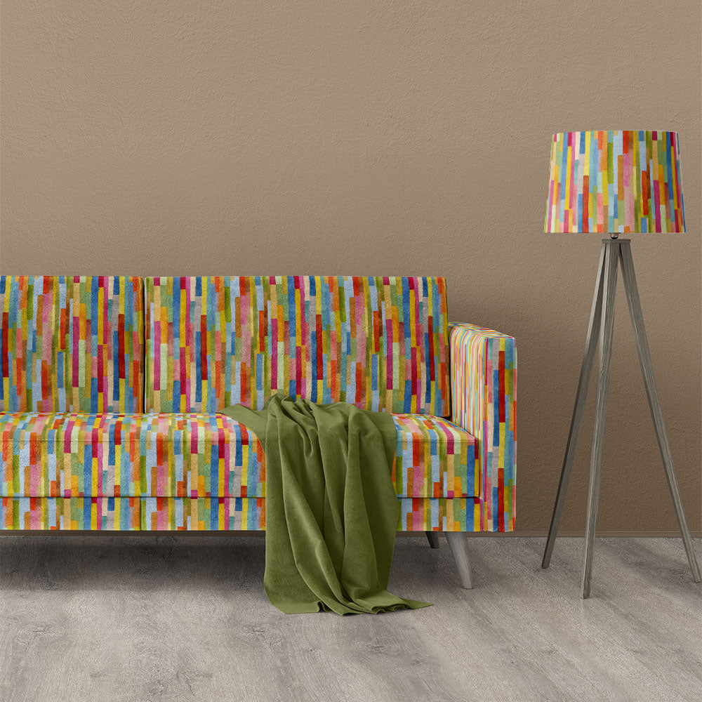 Lakewood striped velvet upholstery fabric shown on a sofa with colourful vertical stripe design