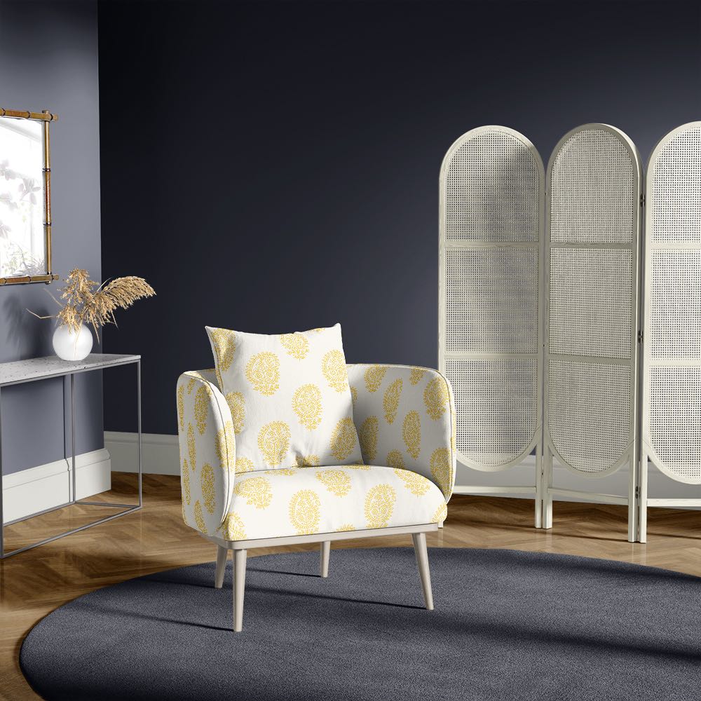 Upholstered chair in paisley ochre yellow upholstery fabric, shown in a dramatic navy room with deep tones and natural wood flooring
