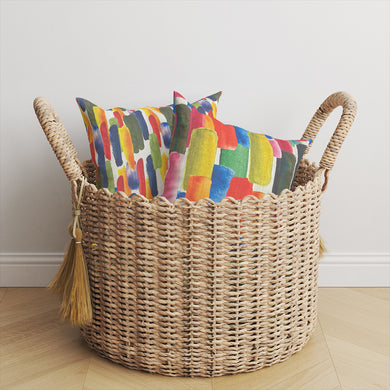 Watercolour Paints linen fabric cushions styled in basket, showing bright multicoloured painterly print on white linen base