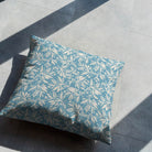 Oxford Leaf Wedgewood fabric styled as a cushion on a grey tiled floor, highlighting the decorative botanical motif.