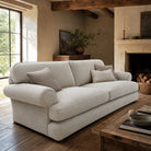 Norton Plain Upholstery Fabric sofa in natural beige upholstery fabric, displayed in a rustic country living room with exposed wooden beams, stone fireplace and warm neutral interior styling.