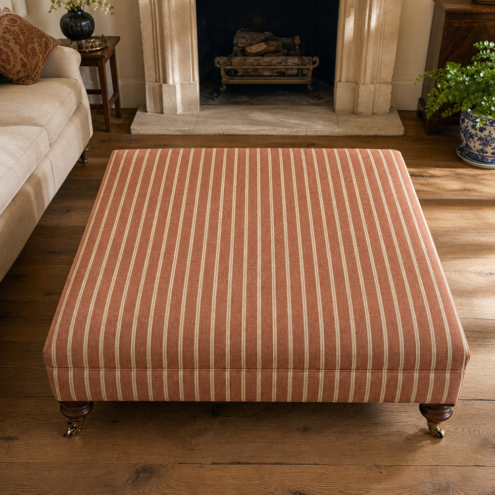 Suffolk Burnt Orange striped upholstery fabric shown on a stool, warm orange cotton-linen stripe for chairs and cushions
