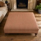 Suffolk Burnt Orange striped upholstery fabric shown on a stool, warm orange cotton-linen stripe for chairs and cushions