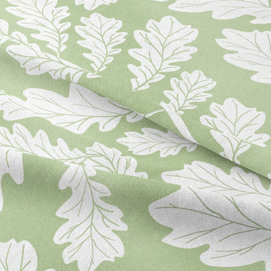  Sage Green Oak Leaf Cotton Fabric swatch draped over a window, showcasing its natural sheen and light filtering properties